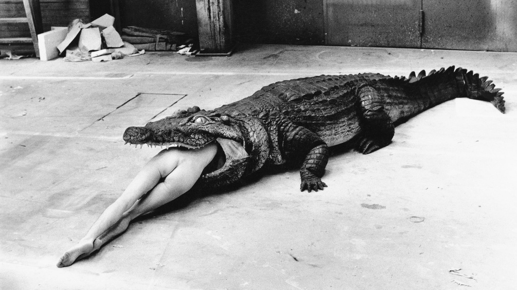 Nackte Frau liegt im Rachen eines Krokodils