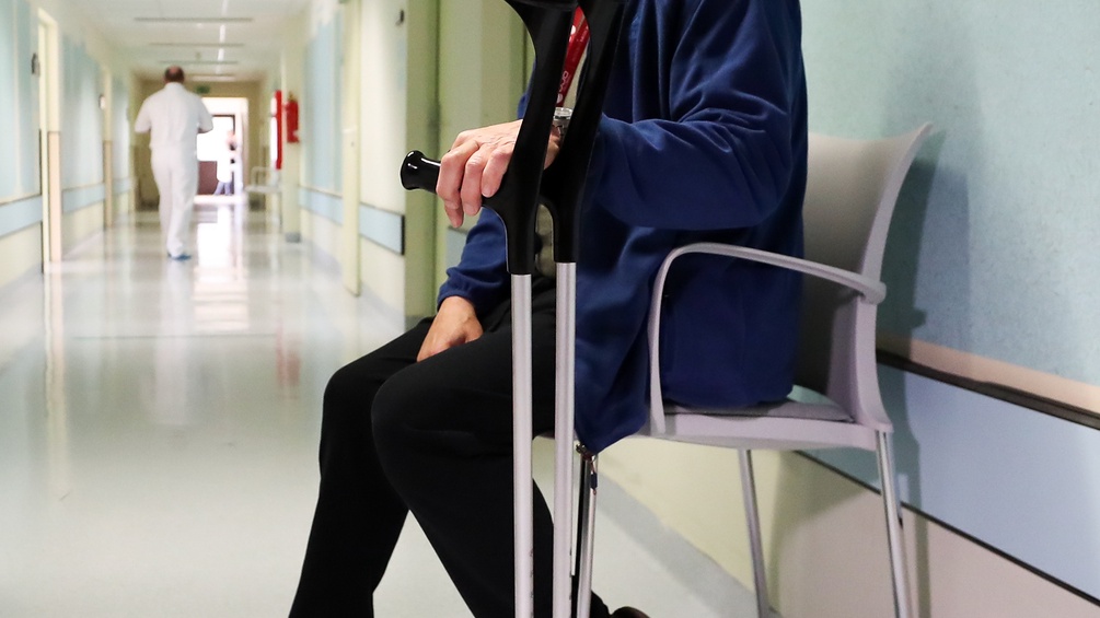 Mann nach einer Hüft-OP auf einer Bank sitzend mit Krücken, Krankenhaus