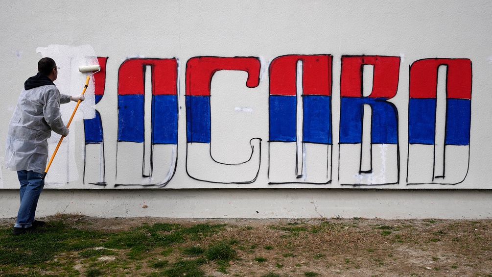 Ein Mann übermalt den Schriftzug "Kosovo" in serbischen Landesfarben geschrieben