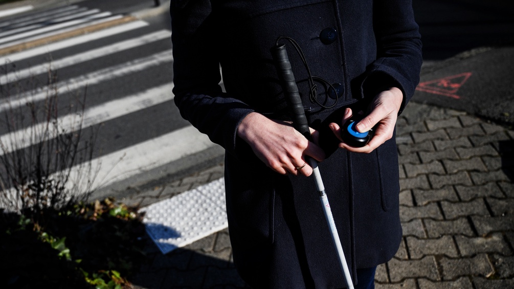 Eine Blinde überquert den Zebrastreifen mit einem Gerät in der Hand.