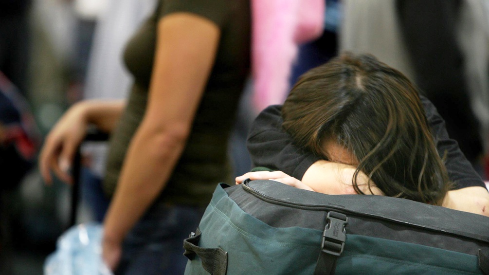 Eine Frau schläft am Flughafen auf ihrem Koffer ein