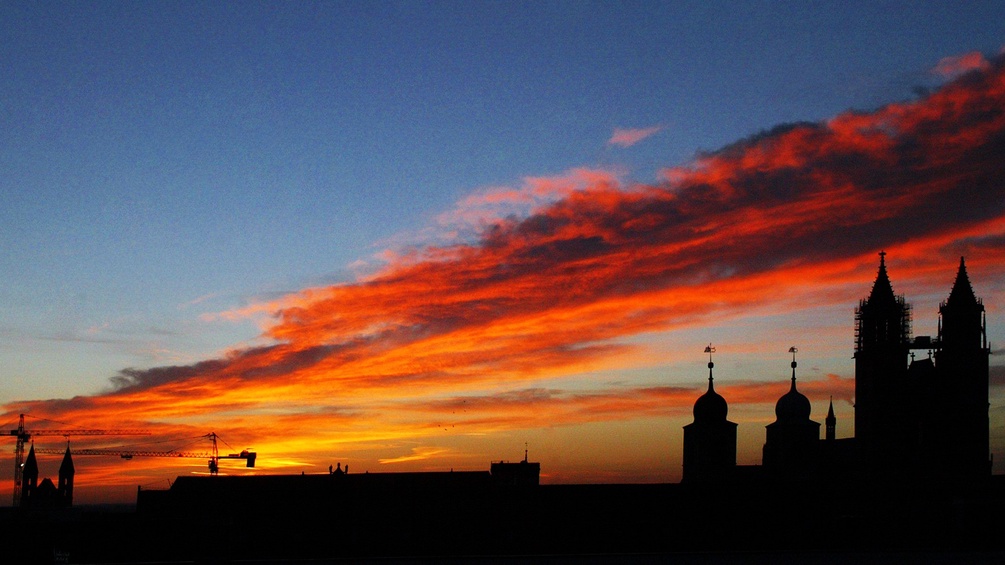 Die aufgehende Sonne lässt den Himmel über der Kirchensilhouette der Altstadt von Magdeburg farbenprächtig erstrahlen.