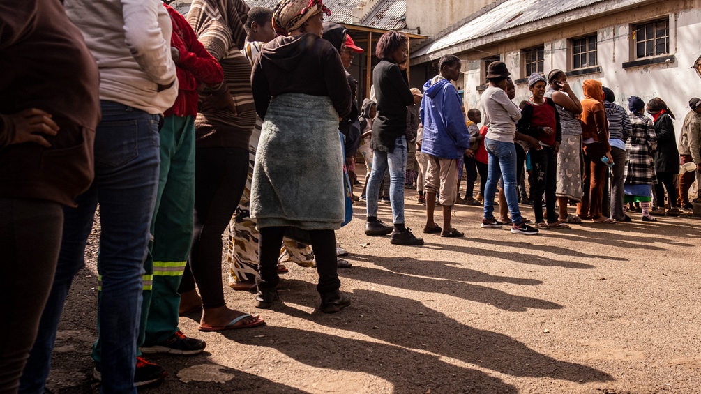 Eine Schlange von Menschen steht in Afrika vor einem Gebäude an.