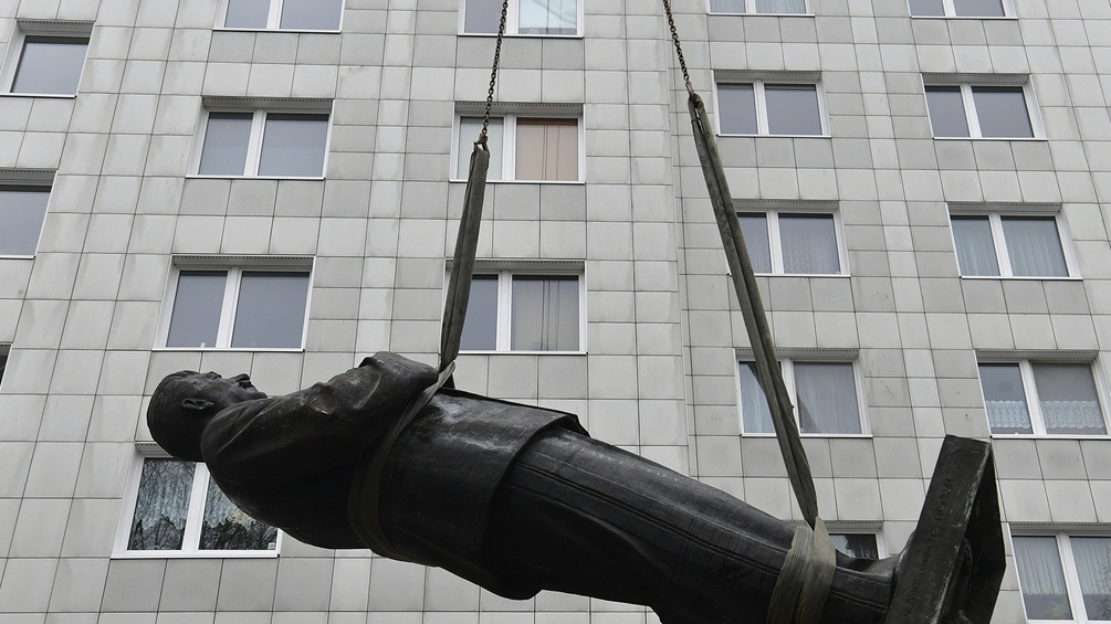 Aine an Seilen befestigte Stalin-Statue schwebt vor einem Hochhaus