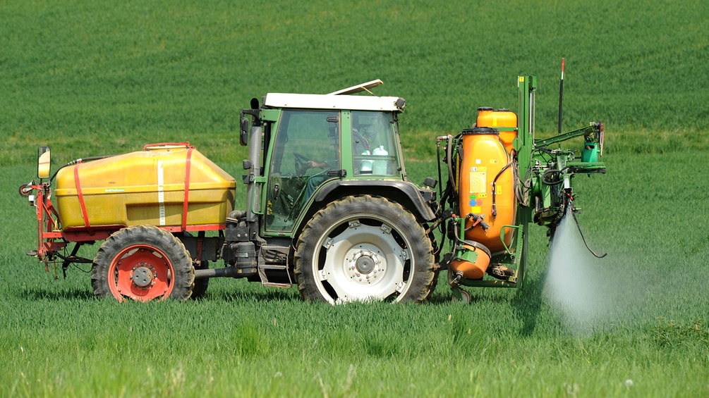 Bauer auf dem Traktor versprüht Pestizide