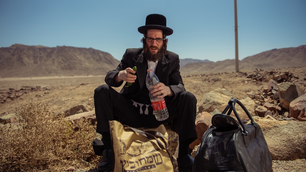 Jude sitzt in einem Wüstengebiet mit seinem Gepäck.