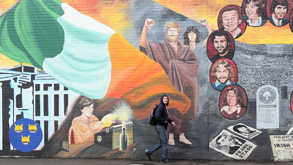 Ein Mann geht an einer Wand mit der Irland-Flagge in der Catholic Falls Road in Belfast vorbei