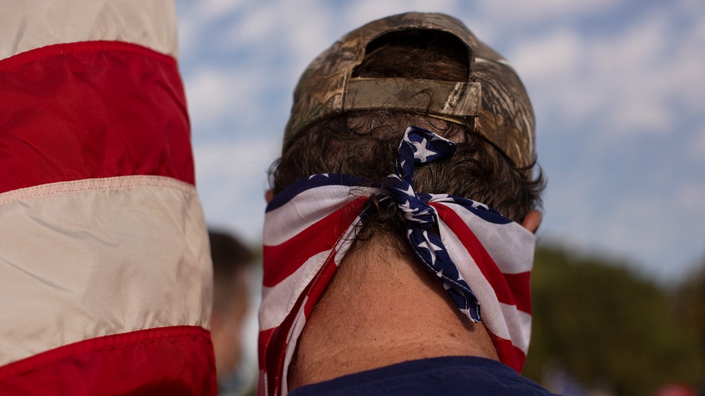 Rückenansicht eines Mannes mit Camoflage-Kappe und US-Flagge