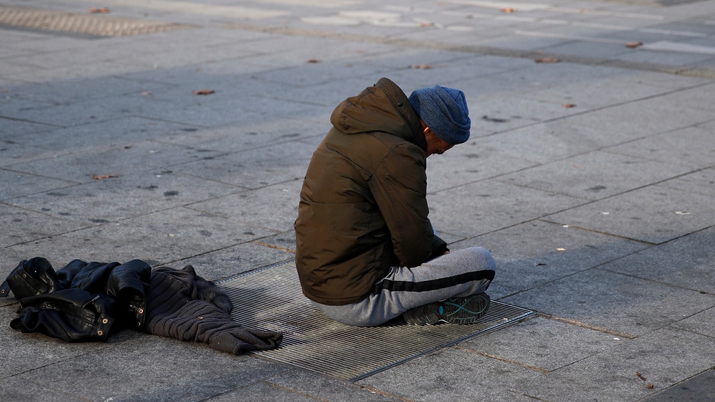 Ein Obdachloser sitzt mit gebeugtem Haupt auf der Strasse
