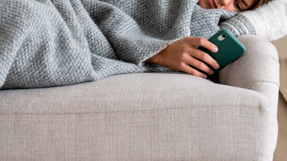 Doom scrolling, Frau mit Smartphone auf einer Couch liegened