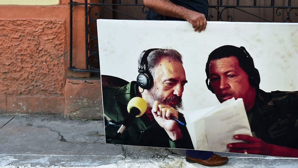 Jemand trägt ein großes Bild von Fidel Castro und Hugo Chavez durch die Staßen.
