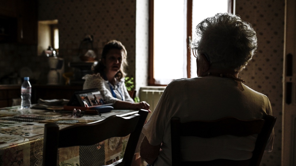 Eine alte Frau sitzt an ihrem Küchentisch mit ihrer Pflegerin