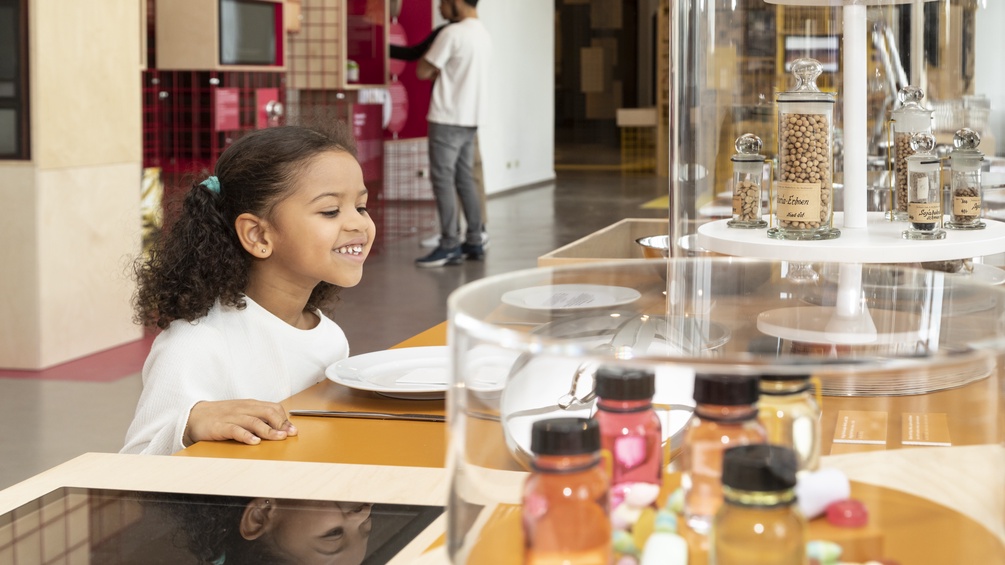 Ausstellungsansicht "Foodprints" im Technischen Museum, junges Mädchen steht vor einem Teller in der Ausstellung