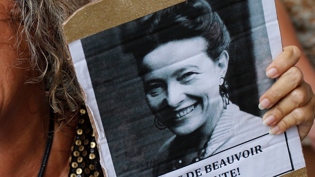 Frau hält Bild von Simone de Beauvoir in Händen