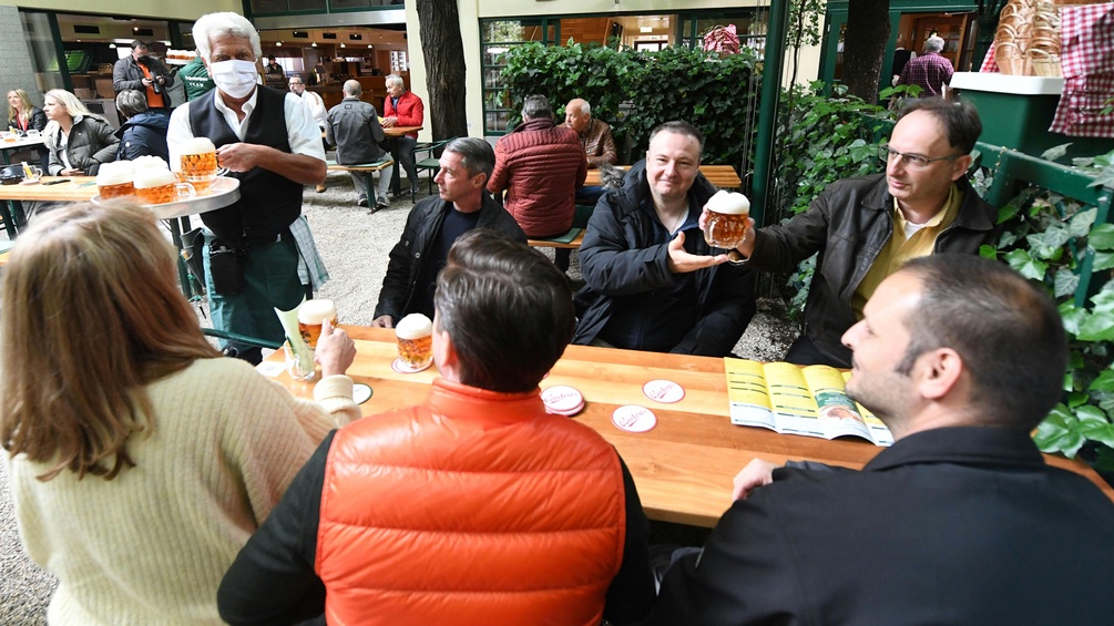 Gäste im Gastgarten eines Lokals trinken Bier.