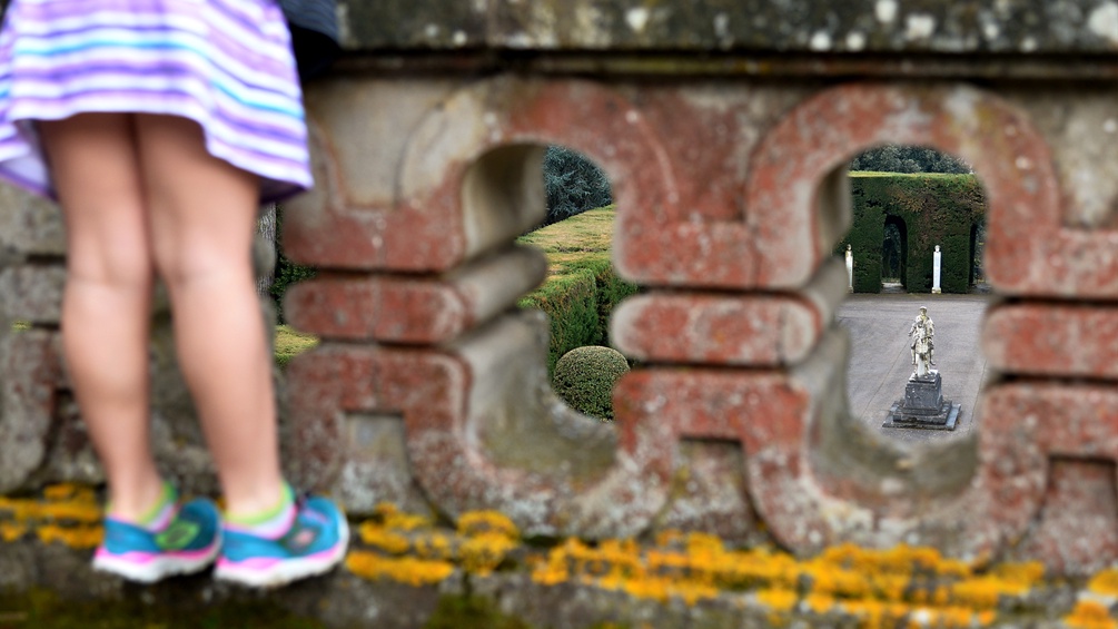Ein Mädchen steht auf einer Mauer und schaut ihn einen Garten.