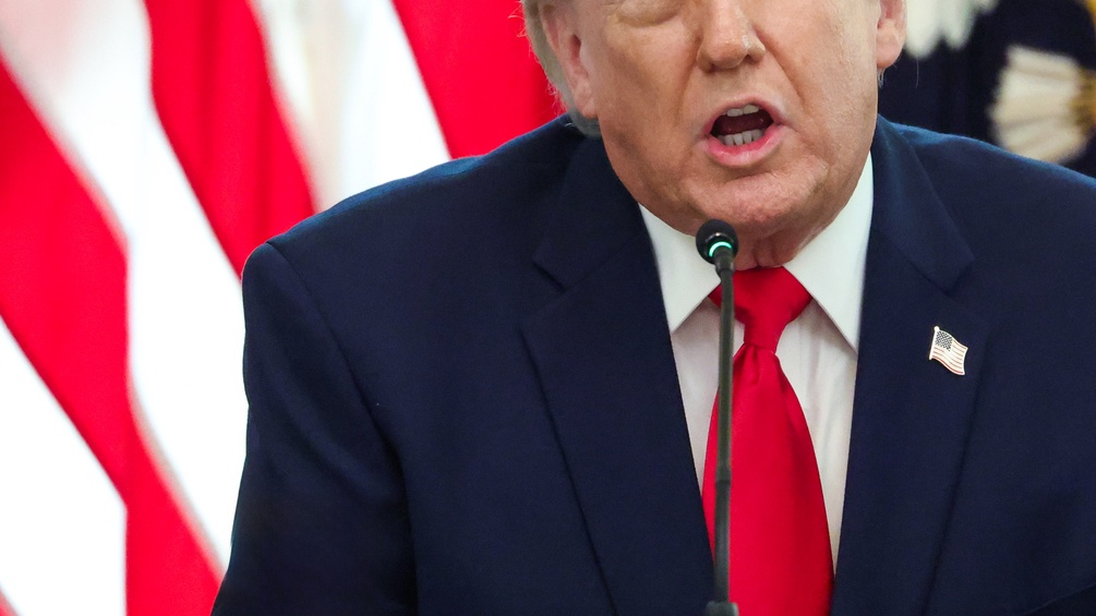 Donald Trumps Oberkörper und Mundpartie, dahinter US-Flagge