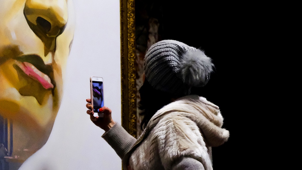 Eine junge Frau fotografiert mit ihrem Handy ein Kunstwerk