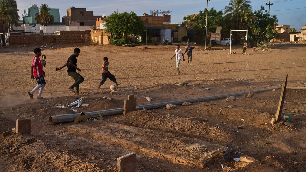 Buben spielen Fußball neben einem provisorischen Friedhof im Sudan