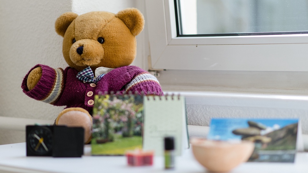 Ein Teddybär, eine Uhr, Duftöl und ein Kalender auf einem Fensterbankerl.