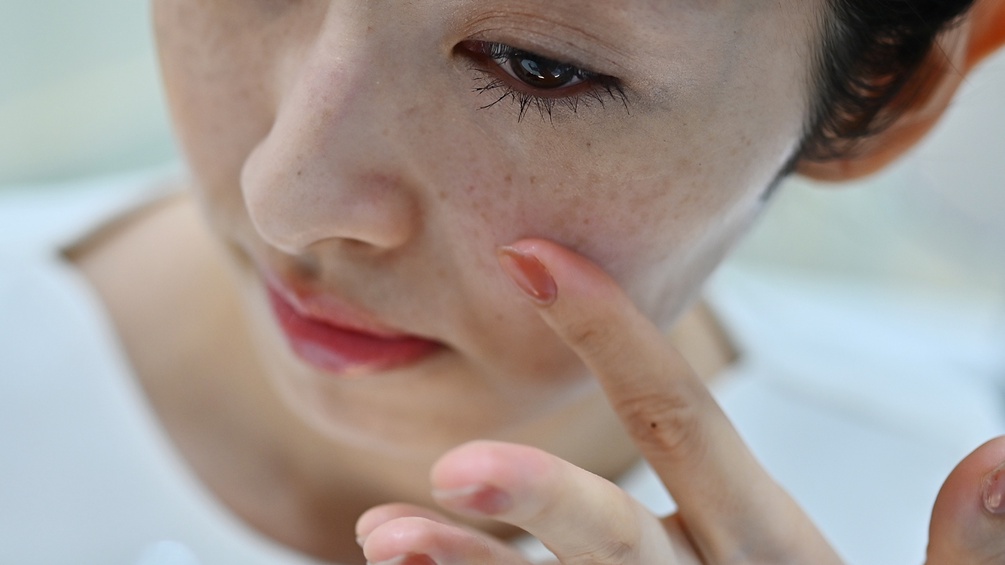 Eine Frau streicht sich die Haut in ihrem Gesicht glatt.