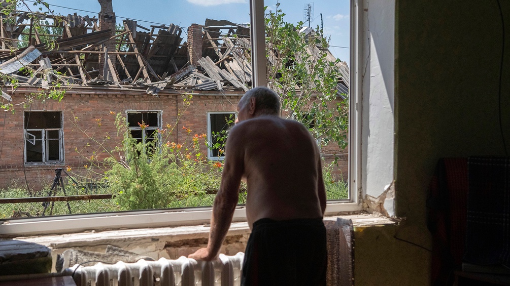 Alter Mann blickt aus dem Fenster, zerstörtes Haus