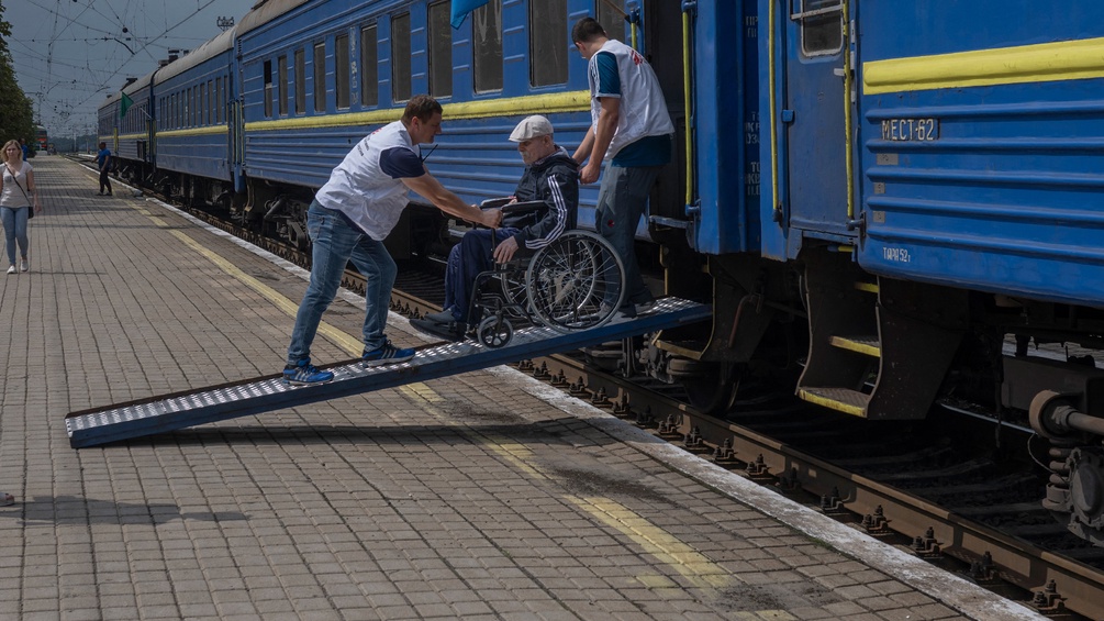 Eine ältere Person im Rollstuhl wird in den Zug geschoben.
