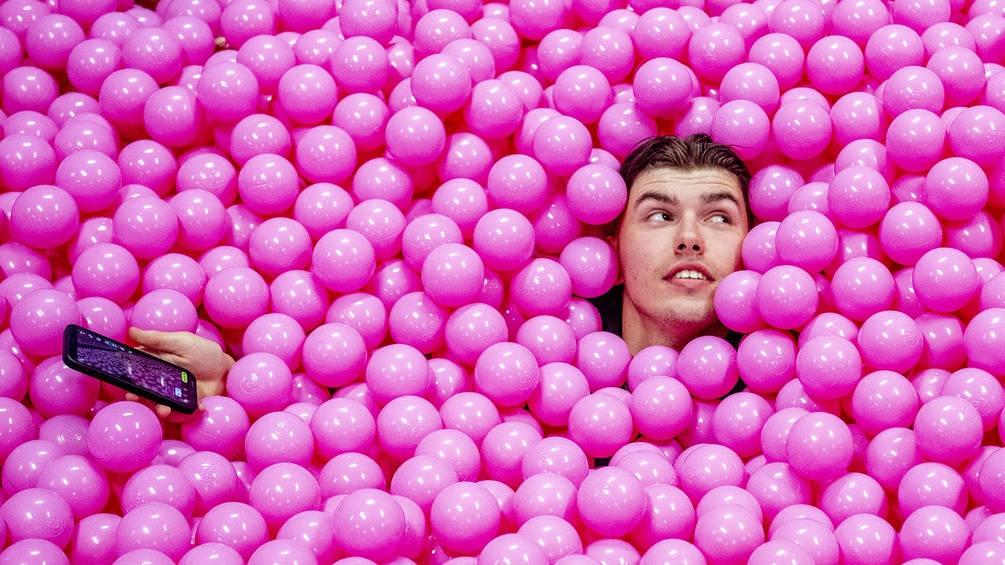 Junger Mann mit Smartphone in einem Bällebad, rosa