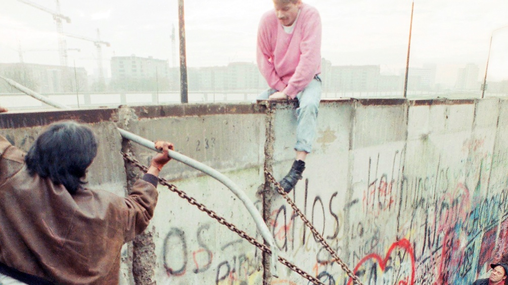Männer klettern über die Berliner Mauer