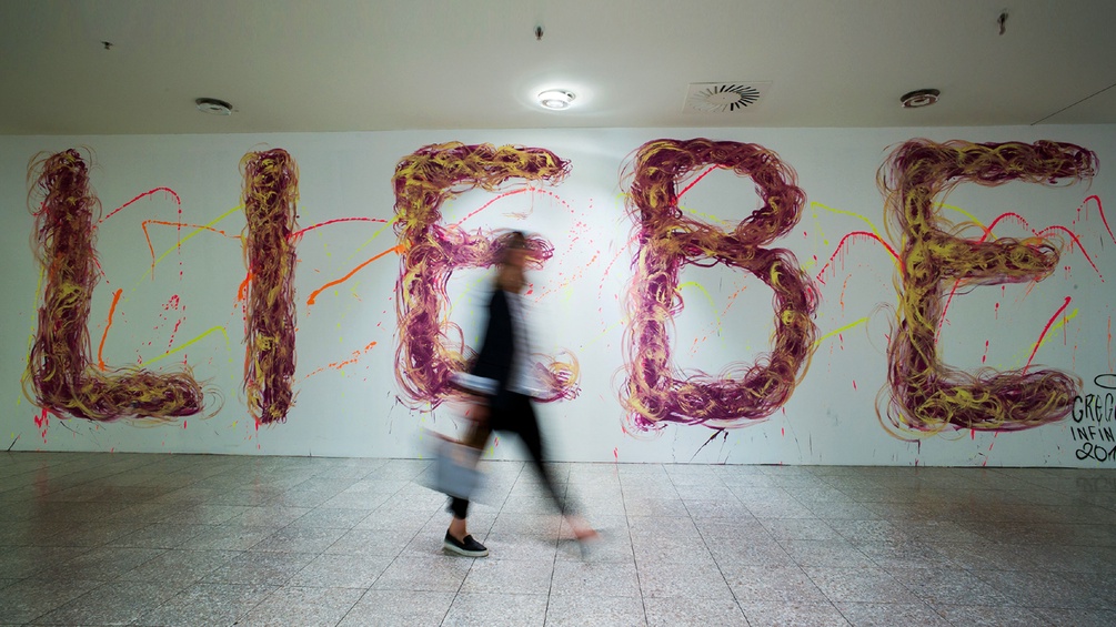Eine Frau geht an einer Wand vorbei, an dem das Wort "LIEBE" in großen Buchstaben steht