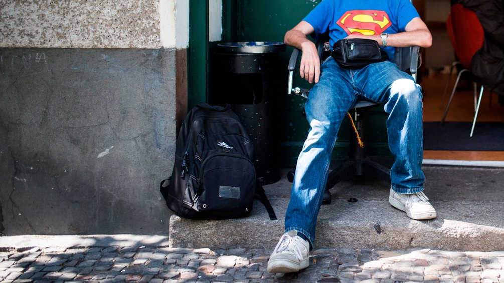 Obdachloser Mann mit Superman-T-Shirt sitzt vor einem Eingang