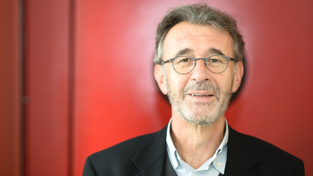 Porträt von Peter Klein vor rotem Hintergrund.