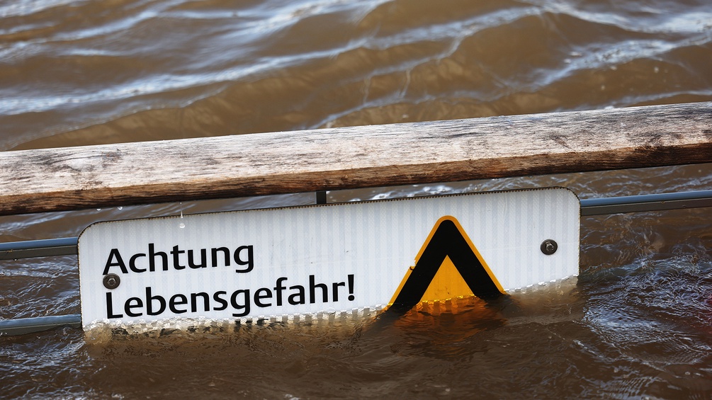 in Warnschild mit der Aufschrift "Achtung Lebensgefahr", das vor dem Schwimmen im Rhein warnt, ragt zum Teil aus dem Wasser.