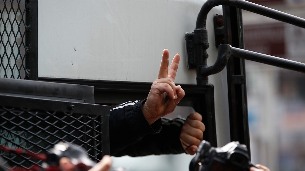 Jemand zeigt ein Peace Zeichen aus einem Polizei Auto heraus