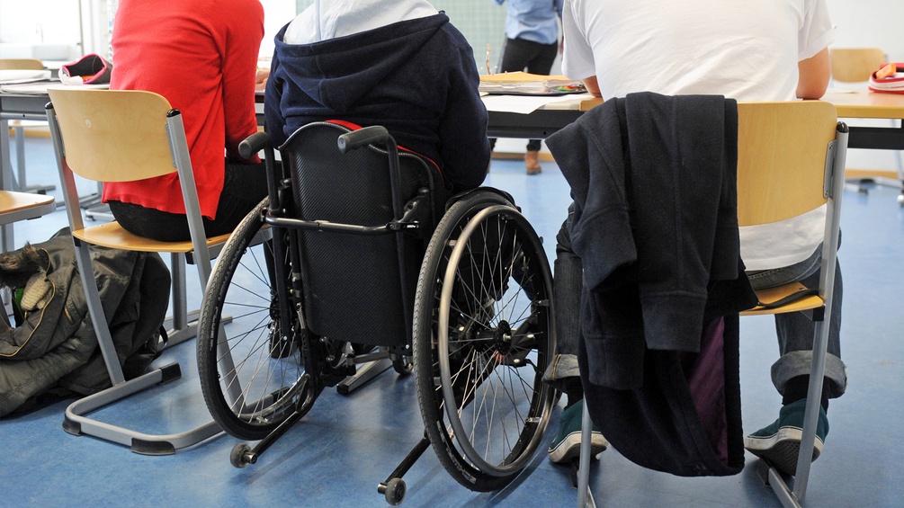 Ein Mensch im Rollstuhl sitzt zwischen zwei Schülern