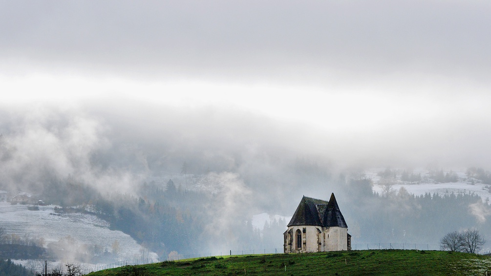 Eine kleine Kapelle steht vor einer frischverschneiten Landschaft