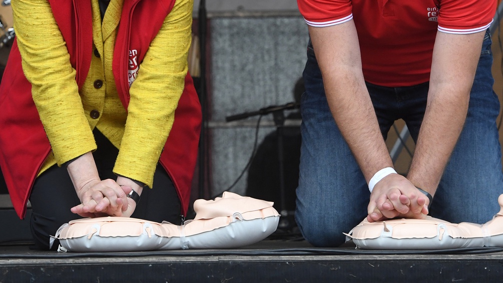 Menschen üben die Herzdruckmassage an zwei Puppen.