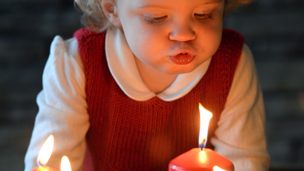 Kleines Mädchen bläst eine Kerze auf dem Adventkranz aus.