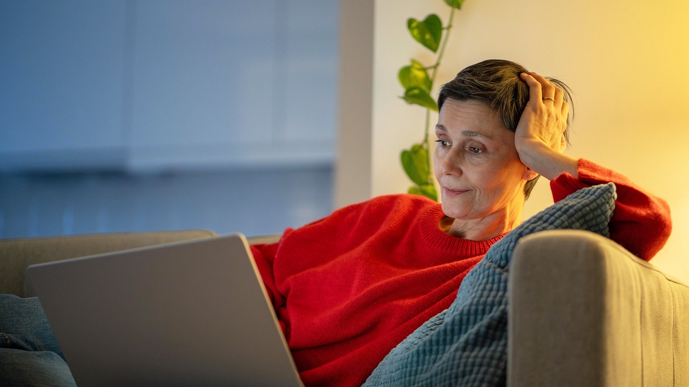 Frau schaut auf einem gemütlichen Sofa in den Laptop