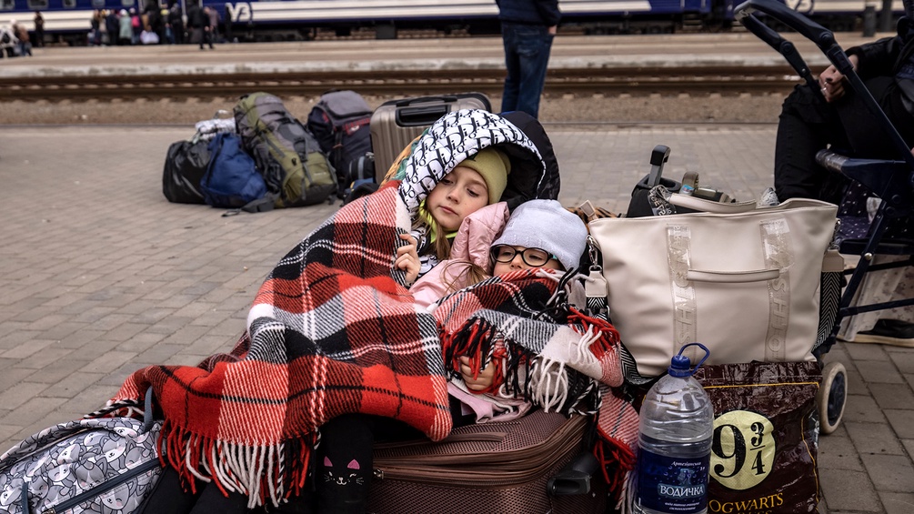 Kinder sitzen auf einem Koffer auf einem Bahnhof