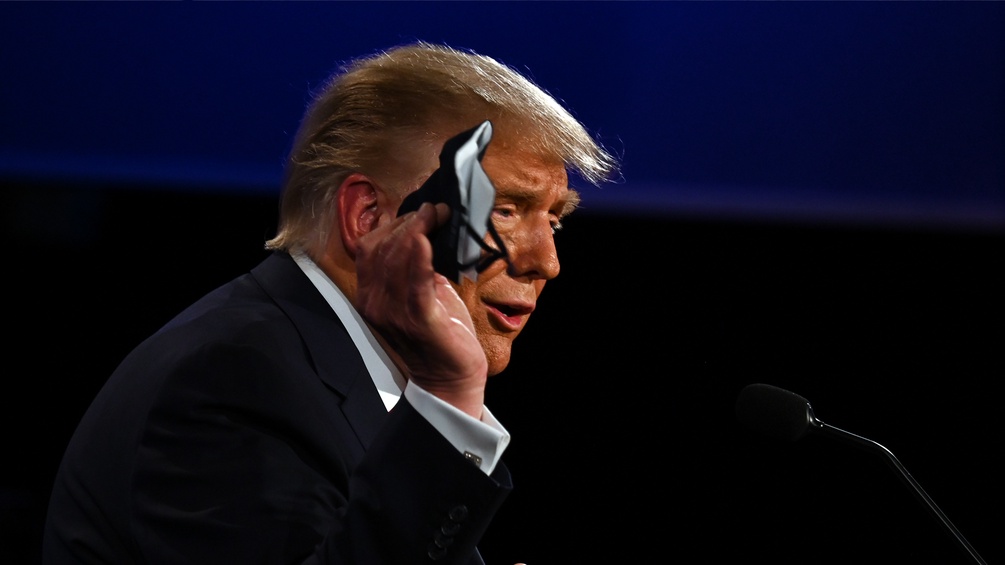 Donald Trump hält seine Maske in die Höhe.