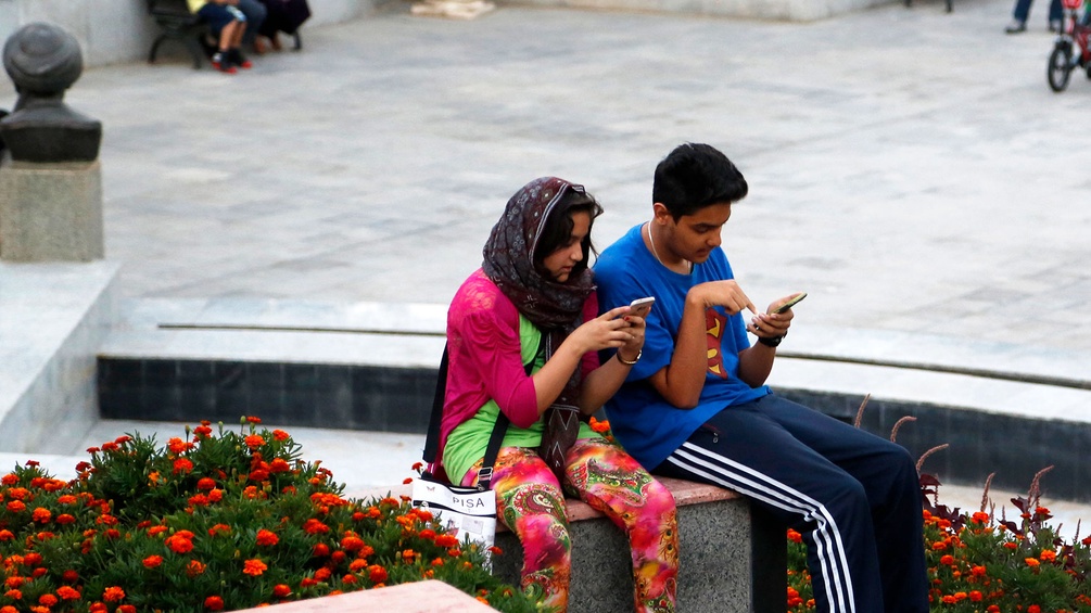 Zwei junge Menschen mit Smartphones in Teheran, sitzend
