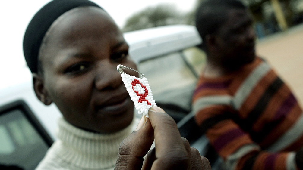 Eine Frau in Botswana hält eine Anstecknadel mit einem Aids Zeichen in die Kamera.