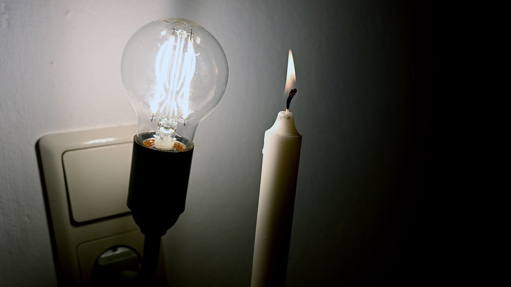Eine Glühbirne steckt an einer Steckdose neben einer Kerze.