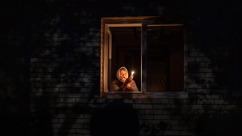 Alte Dame mit Kerze schaut aus einem Fenster in der Ukraine.
