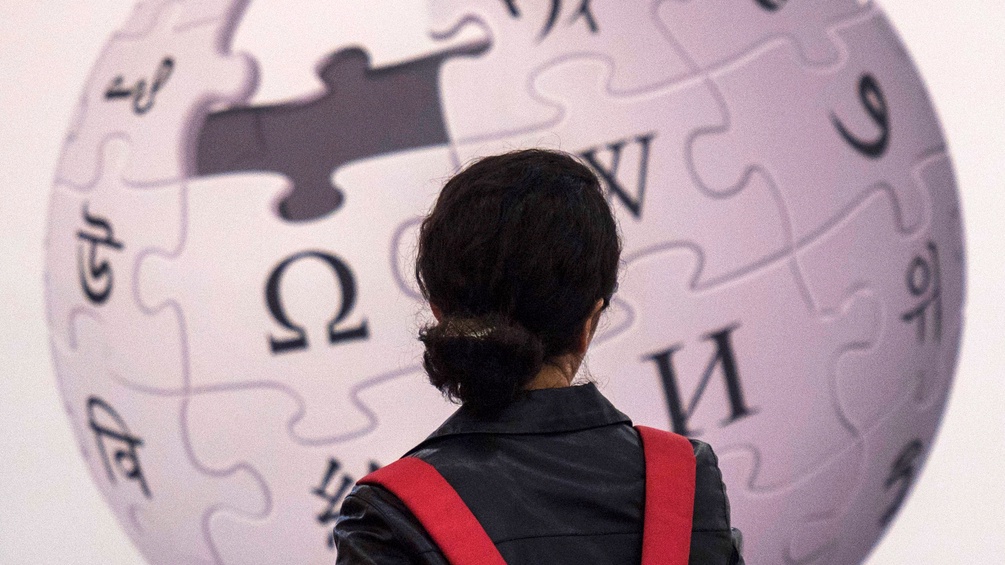 Eine Frau steht vor dem Wikipedia Logo