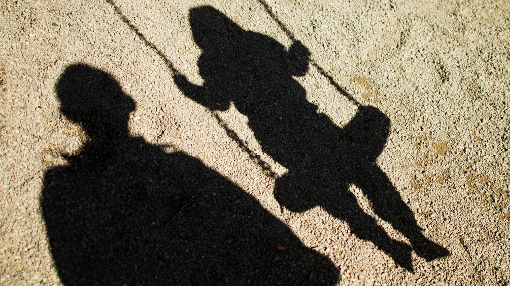 Der Schatten eines Mannes und eines Kindes auf einer Schaukel.