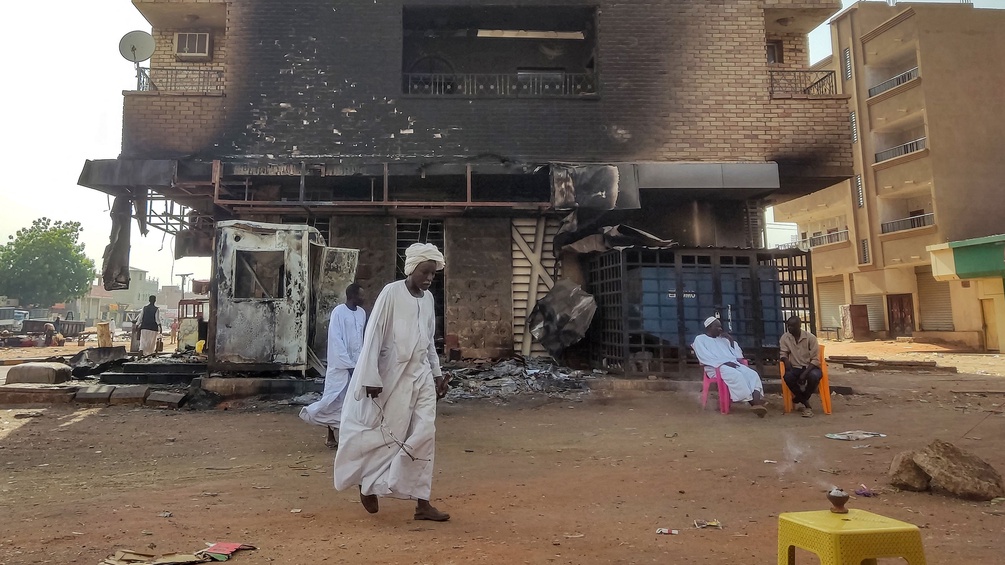 Menschen im Sudan vor einem vebrannten Haus.