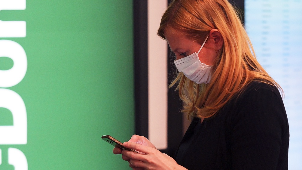 Ein Frau mit Schutzmaske sieht auf ihr Handy