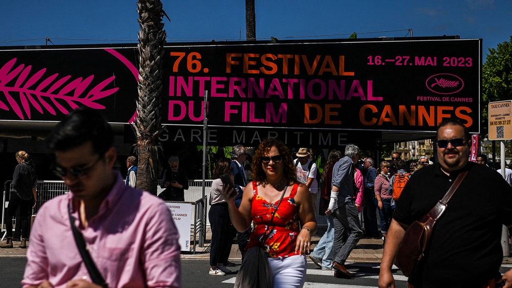 Menschen überqueren eine Straße in Cannes, Banner im Hintergrund